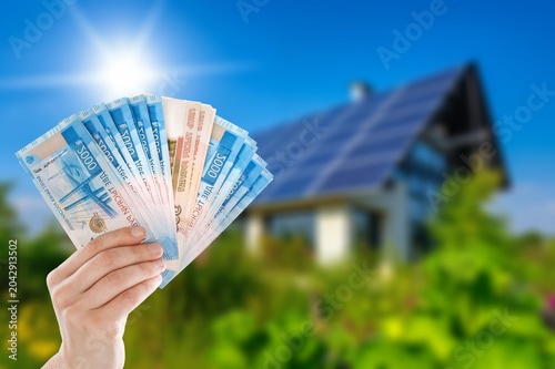 Photos Person holding Russian ruble banknotes in front of house with solar panels