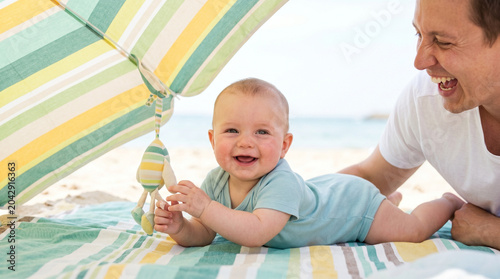 Baby lying under an umbrella and smiling while playing on the beach - Concept of Summer baby birth  