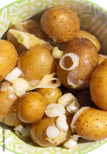 Salad potatoes mixed with spring onions and butter in a green patterned bowl on a white wood background.