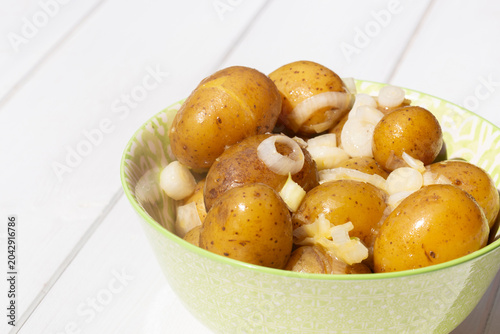 Salad potatoes mixed with spring onions and butter in a green patterned bowl on a white wood background.