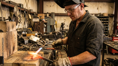 Metal worker using torch to anneal metal in workshop environment  