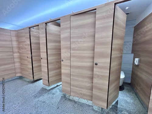 Restroom with multiple toilet stalls featuring light wood grain doors, gray floor, and minimal design.