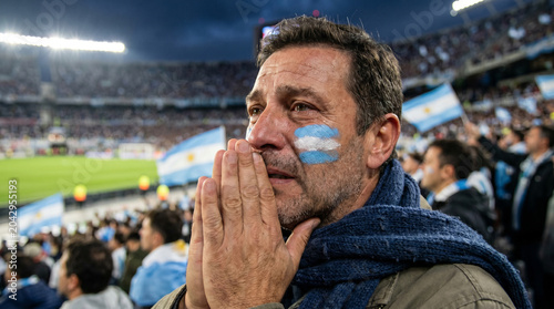 Argentine fan praying with face paint at a crowded stadium during a match