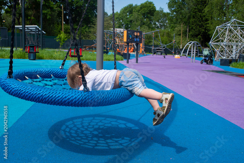  Toddler climbing down from blue round nest swing on playground