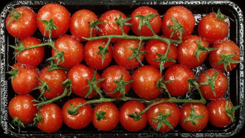 Fresh cherry tomatoes on a black tray with water droplets placed on a table in a kitchen setting