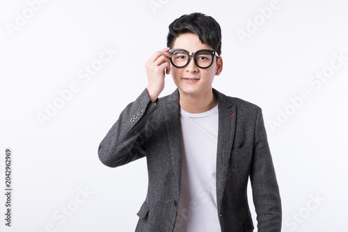 Obraz na plátně Smiling young man adjusting oversized round glasses in studio