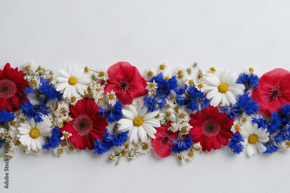Obraz premium An overhead flat-lay arrangement of red poppies white daisies and blue cornflowers celebrates patriotic summer holidays.