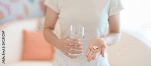 Obraz na plátně woman hand holding medicine painkiller pill and water glass on the sofa at home,