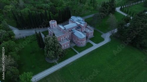 Aerial view of Chateau Mukhrani royal palace and estate in Georgia, magnificent pink castle architecture with a tower surrounded by a lush green park, gardens and pathways on a spring day.