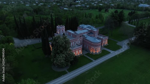 Aerial view of Chateau Mukhrani royal palace and estate in Georgia, magnificent pink castle architecture with a tower surrounded by a lush green park, gardens and pathways on a spring day.
