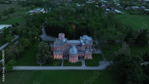 Aerial view of Chateau Mukhrani royal palace and estate in Georgia, magnificent pink castle architecture with a tower surrounded by a lush green park, gardens and pathways on a spring day.