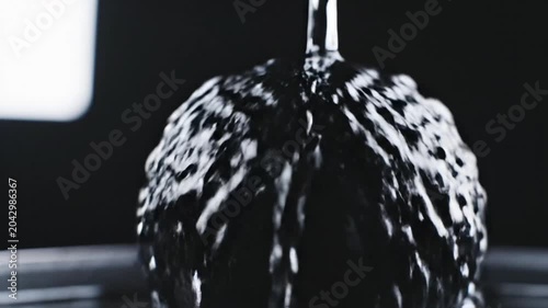 Glossy black liquid pouring with bright white reflections