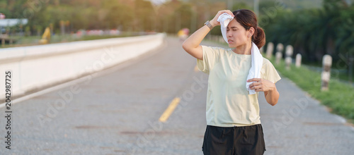 Foto Exhausted Asian woman wiping sweat with a towel after jogging in the park