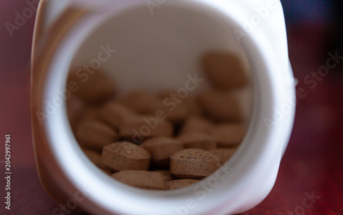 Pills spilling out of a bottle isolated on dark background, Vitamin for health