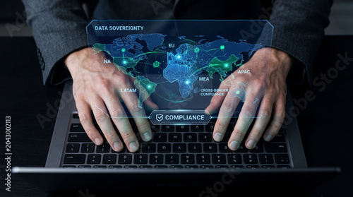 Business professional typing on laptop with holographic world map showing data sovereignty and compliance concepts