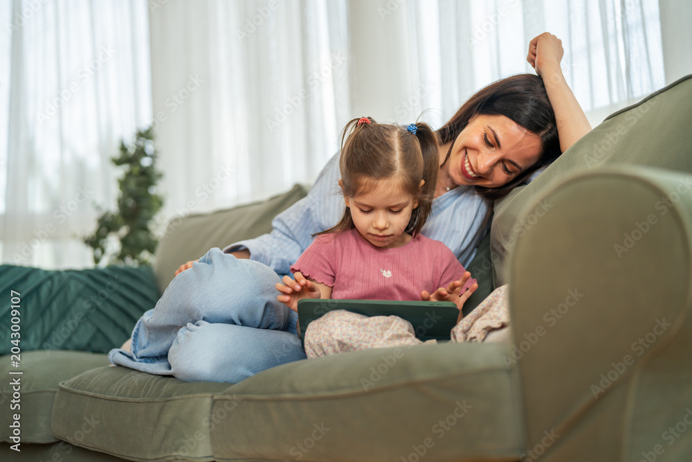 Fototapeta premium Mother and daughter sitting on sofa using digital tablet