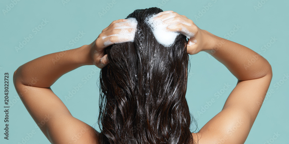 Naklejka premium Woman vigorously applying foamy shampoo to her wet scalp.