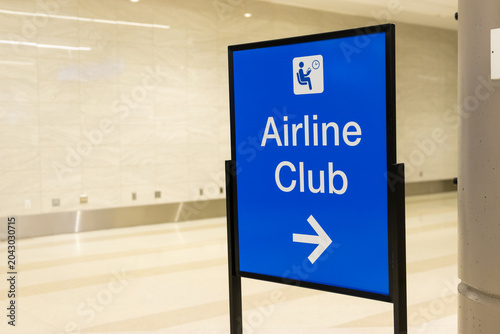 A blue sign at an airport with an arrow to the Airline Club