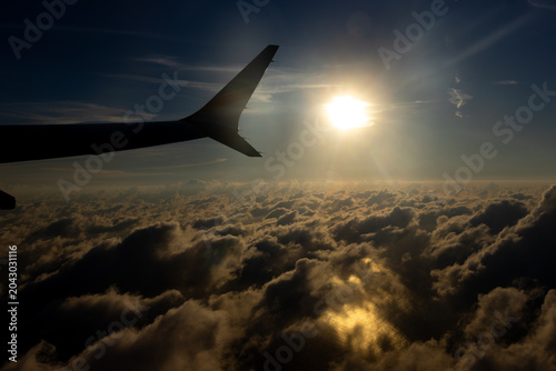 Clouds, sun and an airplane's wing as seen from inside the jet looking out the window.