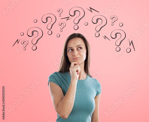 Young woman thinking with question marks above head against a pink studio background