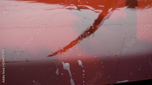 Red car hood covered in foam and grime from regular use. Clean water rinses away residue, restoring smooth surface. Represents effort in maintaining vibrant and polished exterior