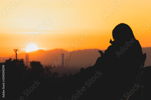 Cuadro en lienzo 夕暮れの景色を背景にスマートフォンを操作する女性