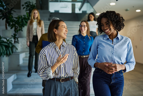 Diverse businesswomen walking and talking in office hallway