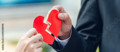 Hand of woman and man in business suit hold split crack red heart paper. broken heart of businessman by show split red heart paper.