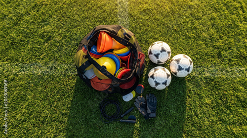 Football training equipment and sports bag on green grass field during sunset