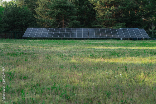 A small solar panel farm for generating eco-electricity on the edge of a forest in a recreation area at the base. Renewable energy, eco-friendliness, and environmental safety.