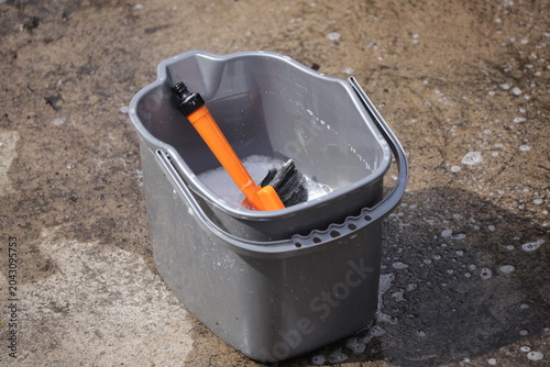 Fotografie Gray cleaning bucket with soapy water and scrub brush on concrete
