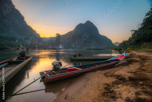Tableau sur toile A pier with fishing boats along the river, situated in a natural setting with a pagoda and mountains