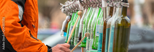 Street musician performing with glass bottles as instruments, showcasing creativity, urban street culture, improvisation, and live public entertainment in a city environment.