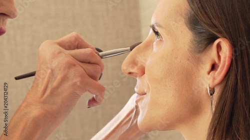 Makeup applying artist, professional beauty routine for a woman, side profile close up with cosmetics brush