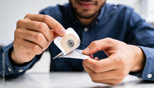 Peeling man in navy shirt removing circular medical sensor patch from sterile foil on white table