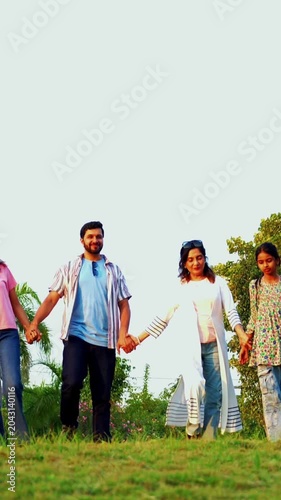 Indian family walking strolling in farm land with green crops outdoors enjoying happy chitchat and bonding moments together, grandparents, parents, and kids spending peaceful quality time in nature