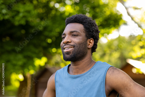 Photos Young man standing outdoors in a park, smiling and looking away, enjoying the su