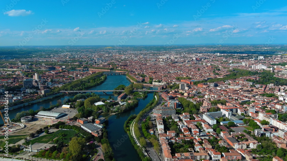 Obraz premium 4K aerial drone image of Toulouse, France. Panoramic summer cityscape featuring the River Garonne and historic red brick architecture.