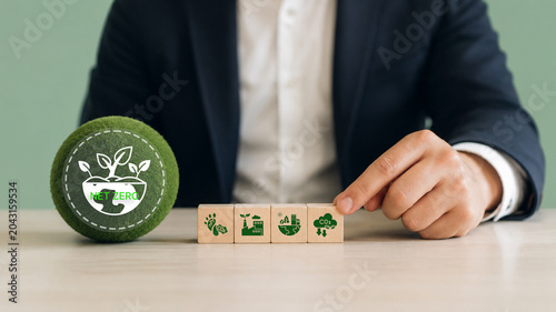 Net Zero, sustainable business strategy concept. Hand arranging wooden blocks with sustainability icons with green sphere labeled 