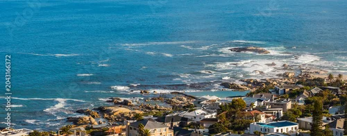 Panel kuchenny z motywem Elevated coastal view shows rocky shore, white surf, coves, and tidal pools by low rise homes near Camps Bay, Cape Town. Clear daylight suggests a calm afternoon.