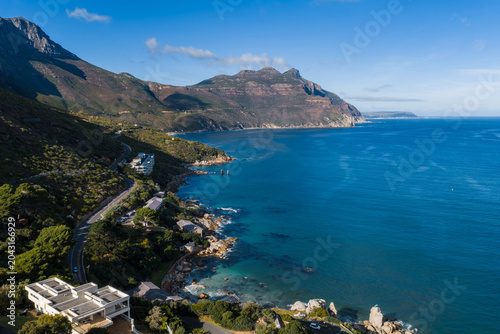 Fotografie Aerial view shows a curving coastal road by Cape Town mountains and bay, with st