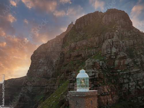 фотографія White lantern lighthouse sits at a rugged cliff base at Cape Point, South Africa