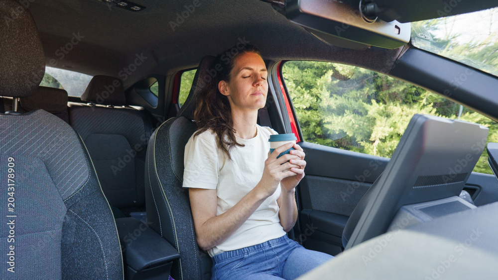 Naklejka premium Woman relaxing in car enjoying coffee break with eyes closed