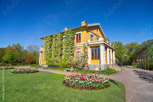 Charming yellow historic house with red tiled roof in lush botanical garden setting, Gothenburg, Sweden