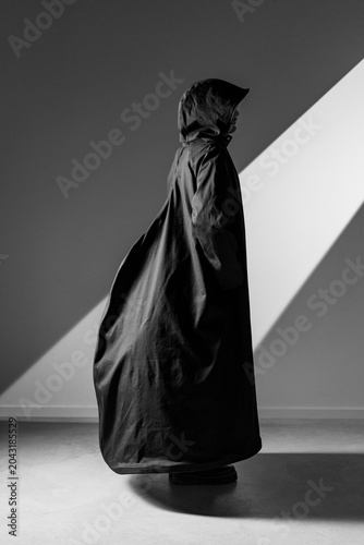 Fotografi Black-and-white portrait of a cloaked hooded figure standing in angular studio l