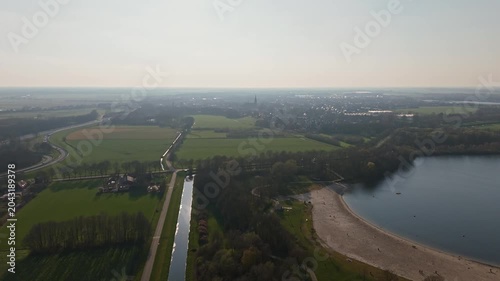 Aerial approach toward Vlijmen town, highway and lake at sunset
