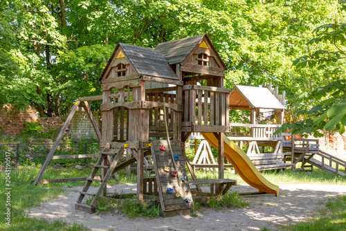 Foto Wooden playhouse with slide and climbing wall in park on sunny day