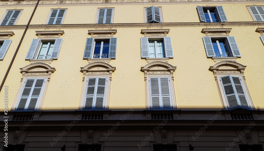 Fototapeta premium A close-up view of a yellow building facade with gray shutters and windows