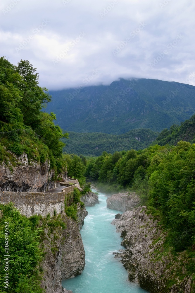 Fototapeta premium Riverside road and misty Soca river in Slovenia surrounded by forest and mountains