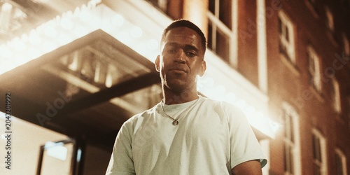 Foto Man in a white shirt stands outside a lit building at night.